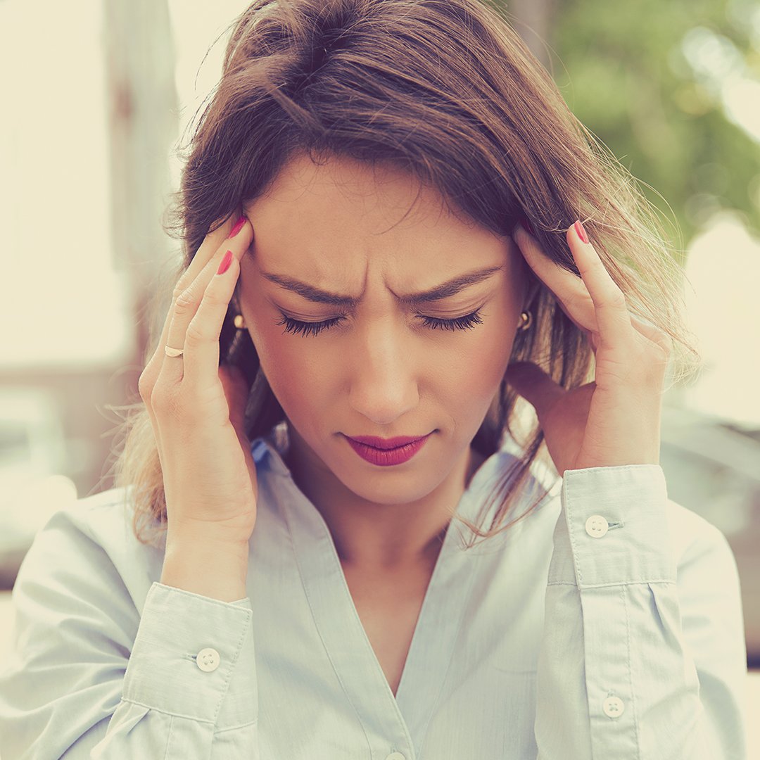 A woman holds her hands to her temples with painful expression
