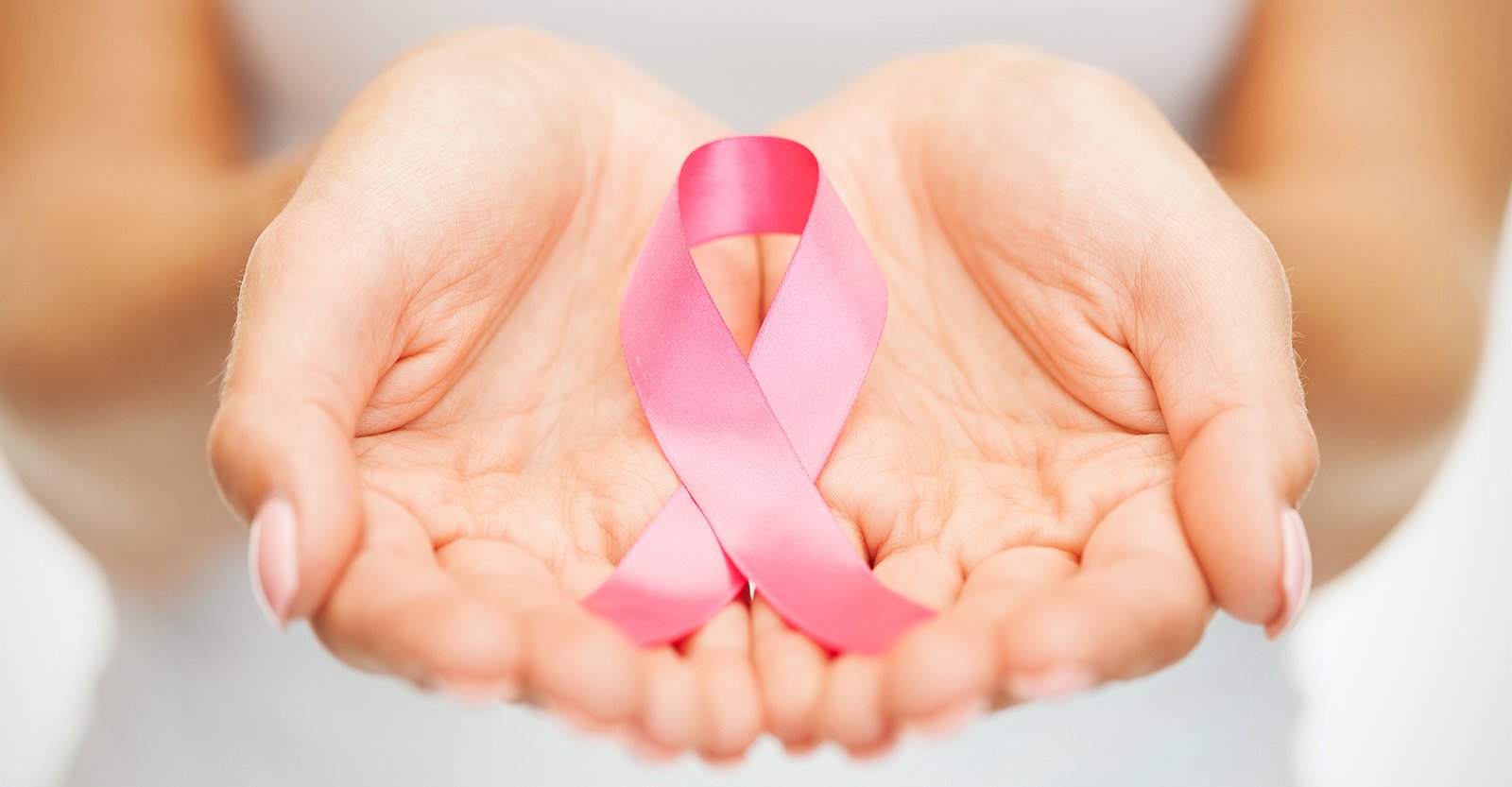 Open hands holding a pink ribbon